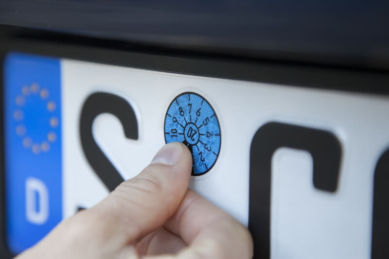 Eine Hauptuntersuchungsplakete, die auf ein Nummerschild geklebt wird